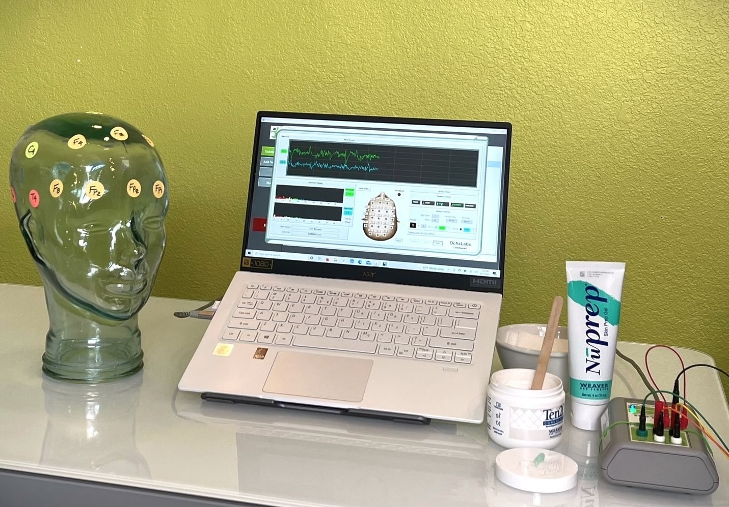LENS neurofeedback setup — head model with electrode placements, laptop with monitoring software